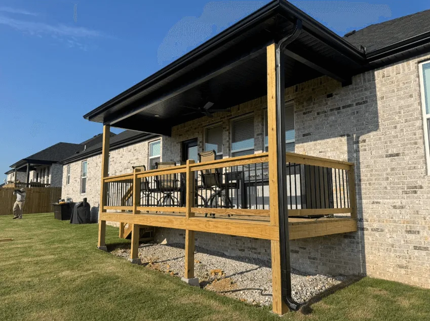 Covered deck with heavy timber posts, metal roof and black balusters attached to a brick home