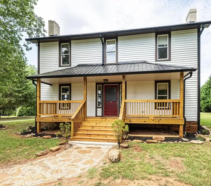 Covered front porch with a standing-seam metal roof, wood railing and steps on a white two-story farmhouse