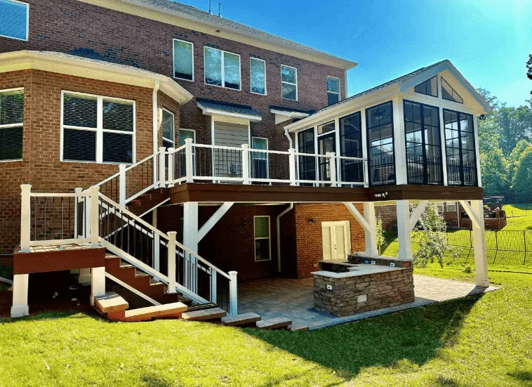 Elevated deck with white railing and open staircase on a two-story brick home with an attached sunroom