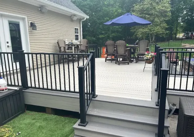Gray composite deck with black railing, descending steps and a furnished dining and lounge area