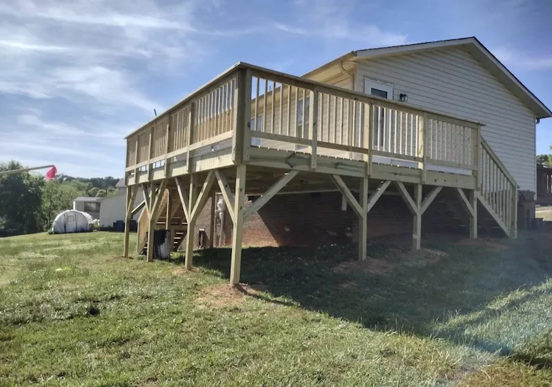 Large elevated pressure-treated wood deck on tall support posts with a long staircase to the yard