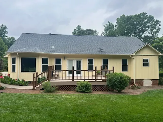 Low-profile deck with brown posts, black balusters and lattice skirting running the length of a ranch home