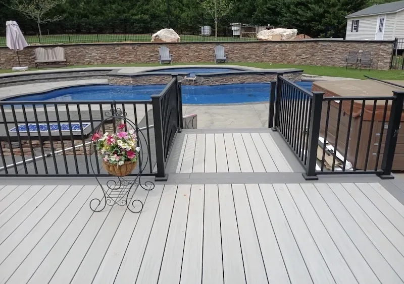 Light gray composite pool deck with black metal railing and gated access to an in-ground pool and spa