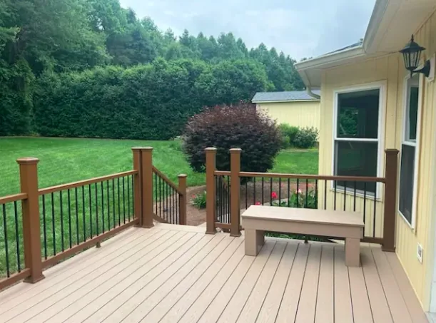 Tan composite deck with brown posts, black balusters and built-in bench seating overlooking a sloped back yard